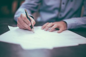 homme écrivant une lettre sur du papier avec un stylo